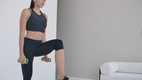 Close-up-young-beautiful-brunette-woman-steps-on-a-chair-with-dumbbells-in-her-hands.